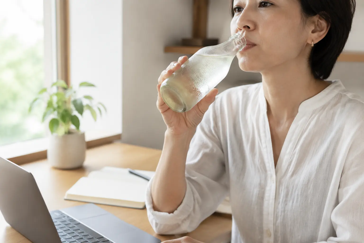 仕事の合間に冷たいガラスボトルで水分補給する様子